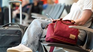 Cestující sedí v hale s příručním zavazadlem 