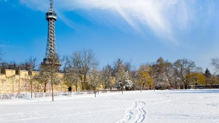 Zasněžený park s Petřínskou rozhlednou v pozadí.