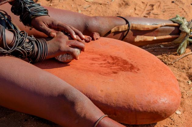 Ruce ženy kmene Himba připravující červenou hlinku na pastu otjize.