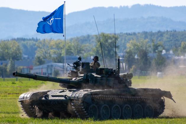 Pásový tank T-72 s alianční vlajkou projíždí po travnaté ploše