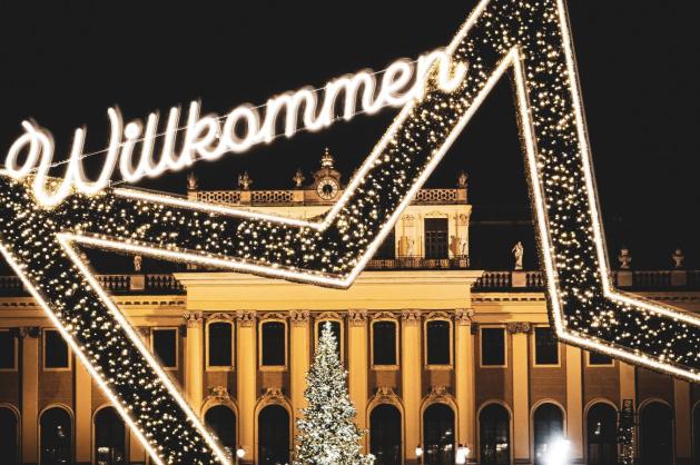Osvětlená brána „Willkommen“ před barokní kulisou Schönbrunnu