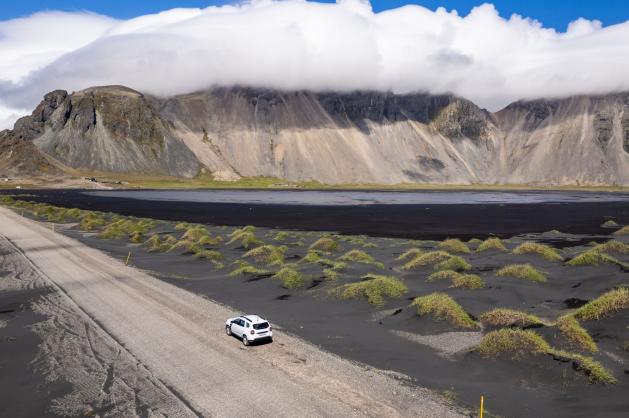 Osamělé auto projíždí krajinou černého sopečného písku 