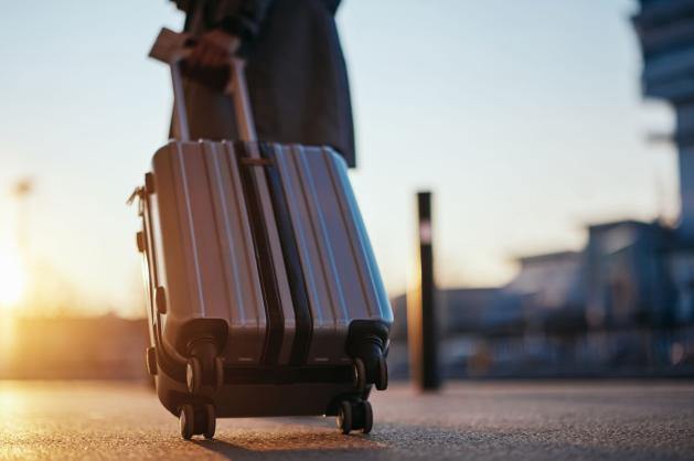 Cestující s kufrem stojí na letištní ploše 