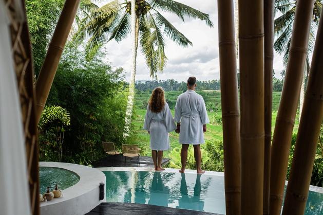 Pár v županech stojící u bazénu s výhledem do zelené krajiny 
