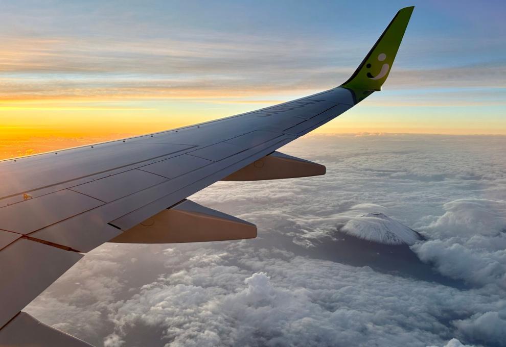 Křídlo letadla osvětlené ranním sluncem nad vrstvou oblaků.