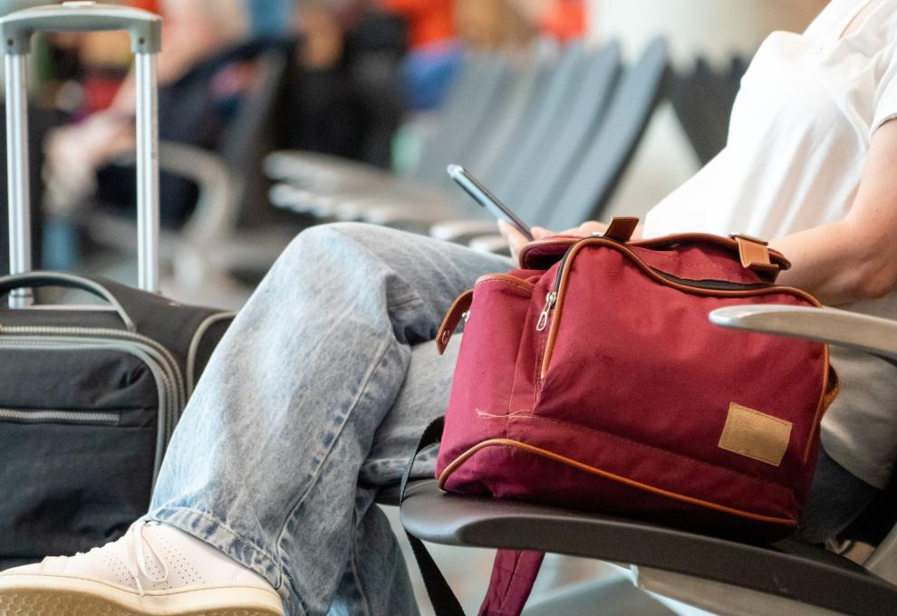 Cestující sedí v hale s příručním zavazadlem 