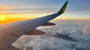 Křídlo letadla osvětlené ranním sluncem nad vrstvou oblaků.