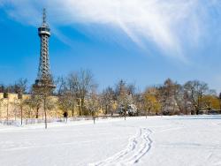 Zasněžený park s Petřínskou rozhlednou v pozadí.