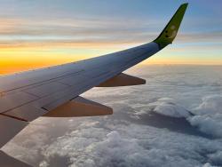 Křídlo letadla osvětlené ranním sluncem nad vrstvou oblaků.
