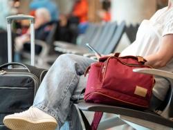 Cestující sedí v hale s příručním zavazadlem 